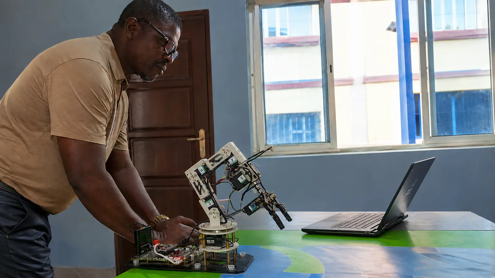Petra Academy instructor demonstrating a robotic arm beside a laptop